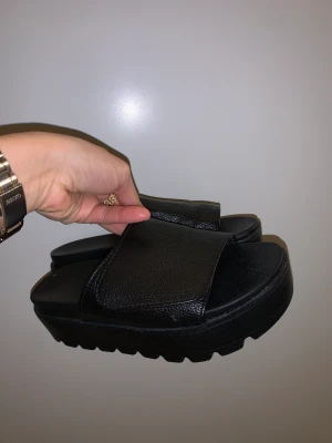 Svarta slip-ins. Storlek 38 - Svarta tofflor med platå i skinnimitation. Med kadborreband för justering. Älskar men är för små tyvärr... Storlek 38 men känns som en 37!  🌱