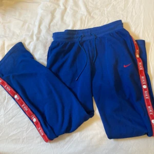 Nike byxor - Blåa Nikebyxor med röda detaljer. Knappar längs sidorna av benen. Jättebekväma och endast använda fåtal gånger. Skriv för bilder på💓Är storlek 38 men passar mig som har 36