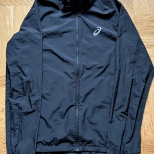 Asics jacka - Vind/löparjacka från Asics. Använd 1-2 gånger då jag köpte en storlek större istället.  Storlek small 