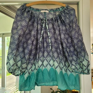 Blus i blått och turkost av claire.dk, M - Blus med dragsko i halsringningen och lite puffiga ärmar. Blå, vit och turkos, storlek M. Fint skick. 