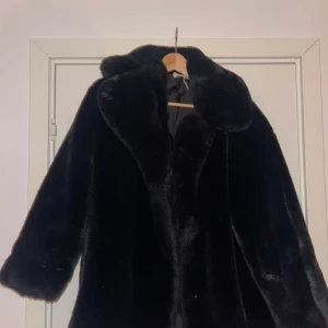 Fuskpäls - Svart fuskpäls från Mango. I gott skick förutom öppningarna vid ärmarna där pälsen har ”tovat sig”, se andra bilden.