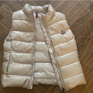 Moncler Väst 134-XS - En väldigt fin ljusare beige Moncler väst, bilden ovan är lånad. Säljer pågrund av att den helt enkelt är för liten på mig. Passar även XXS samt XS. Fint skick inga skador osv. Inget bestämt pris, det kan diskuteras. kom privat för andra frågor ☺️ 