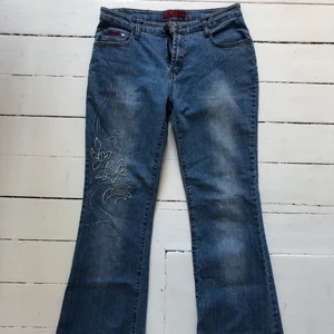 Lågmidjade jeans med broderi  - Snygga lågmidjade jeans med en broderad blomma. Jeansen är utsvängda. Köpt second hand. 