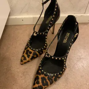 Svarta klackskor från Michael Kors med detaljer i leopardfärgat tyg samt guldiga ”dubbar” Storlek 6M (storlek 36) Klackhöjd ca 10cm  Använda endast två gånger, i bra skick. Kostade 1500kr men säljs nu för 799kr.