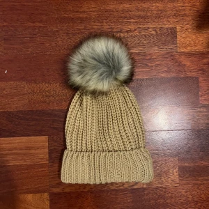 Mössa  - En beige mössa med fluffig boll på! 