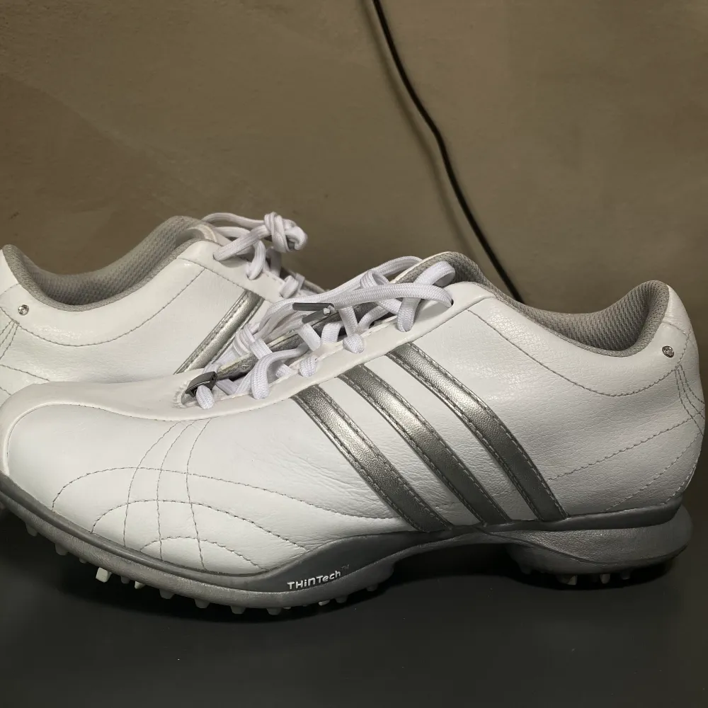 Ovanliga golfskor i storlek 38 från Adidas i färgen vit. Har små kristaller på skorna. Är i fantastiskt skick, bara använda en gång. Saknar tyvärr lådan, därav priset. Kommer att rengöras innan frakt. Öppen för bud!. Skor.