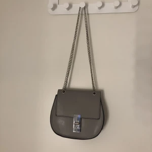 Rymlig handväska  - En liten väska med måtten (höjd: 17cm  bredd: 19cm). Den är välanvänd och har därför några skråmor, men inga som påverkar väskans funktion! Den rymmer mycket trots sin storlek!