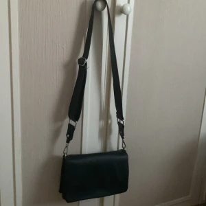 Liten svart väska - Säljer denna fina väska då jag tröttnat på den. Använd under sommaren och inte använd sen dess så i fint skick! Tre stora fack där en av dem har dragkedja, litet fack inuti en av facken och en magnetknapp för att stänga väskan! Nypris: 399kr