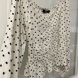 Prickig topp - En prickig topp från Bikbok. Med drapering framme och volanger. Lite croppad och lågt under axlarna. Sitter jätte fint och lite figursydd i midjan. Lite större på armarna och sedan slutar med fina volanger. Använd en gång därav helt nytt skick.
