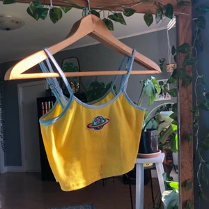 Gult linne med tryck - Ett gult gulligt linne med blå kant och en liten jordglob fastsydd, justerbara band och smått stretchig. Ursäkta fläcken, tvättade tröjan efter detta.