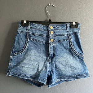 Highwaisted jeansshorts från Gina Tricot  - Highwaisted jeansshorts från Gina Tricot med knäppning och dragkedja. Flätdetaljer! Lite slitna i färgen då de är några år gamla men är supersöta och annars gott skick 