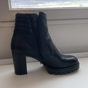 Stövletter fodrade strl 39 - Ilse Jacobsen, svarta stövletter, strl 39, normal storlek. Använda inomhus en dag. Hög klack, 8 cm, sula fram 1 cm. Fint skick! Väldigt snygga och mjuka.