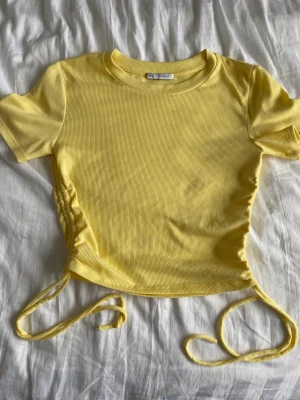 Gul T-shirt med dragsko - Den sitter relativt normalt, något högre i halsen. Dragsko på sidorna och ett ribbad material✨