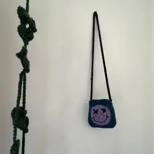 Unique mini bag crocheted by hand. Blue and purple on one side, different shades of green on the other. Both sides have a smiley face design. Knitted i-cord strap! Perfect for the upcoming spring season!💜