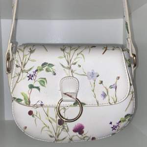 En vit väska med blommor på säljs. Väskan är oanvänd. Säljs för 95kr. Rek pris 150kr. (Priset kan diskuteras) 