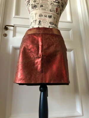 Skinnkjol, minikjol, metallic - Skinnkjol från märket Le Complici i metalliska röd-bruna färger. Väldigt unik med snörning fram (eller bak?), low waist! Storlek M men funkar på S också ☺️<3