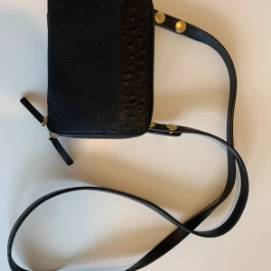 Blankens THE MONTAUK MIDI BLACK GRAIN - THE MONTAUK MIDI BLACK GRAIN Kanonfin väska från Blankena som tyvärr inte kommer till användning här. Tidigare modell som inte finns kvar i sortimentet längre. Gjord av läder.   h: 12  cm, l: 18  cm, w:  4 cm.  Strap length: 126 cm.