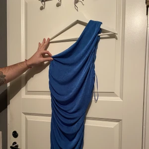 One off shoulder glitterklänning storlek M - Oanvänd klänning från Fashion Nova i storlek M. Liten i storleken. Är i en glitter-blå färg & one off shoulder. Perfekt till nyårsfesten! 