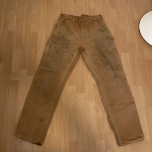 Carhartt double knees 32/34 - Plagget är i gott skick med lite fläckar här och där (främst på vänstra benet. Se bild 2) vilket ger en vintage look. Byxorna har inga hål. Säljes då de är för små.