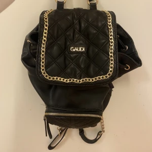 Väska - !Intresekoll! En gaudi ryggsäck nästan nyskick förutom en slitning på bandet längst upp (se bild 3) den är i läder med guld detaljer (inte äkta guld) den är köpt i Italien och går inte att få tag i längre (nypris 1500) det är även ställbara band