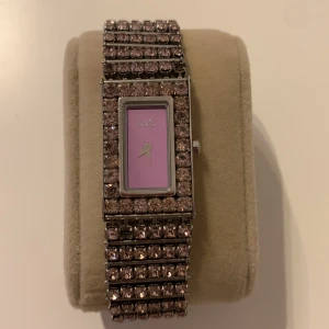 DOLCE & GABBANA SWARIVSKI CRYSTALS WATCH D&G - DOLCE GABBANA D&G klocka med rosa swarovski crystals stenar, några saknas men det syns knappt.  Mått runt 15cm Behöver nytt batteri  Nypris 4000