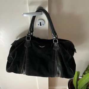 Zadig & Voltaire väska - Zadig et Voltaire Sunny bag i större modell. Väskan är i svart mocka med vissa svarta läderdetaljer. Den har används en del och vissa mockapartier är därför lite slitna, men det går säkert att fixa med en mockavätska och väskan är i helhet i bra skick.