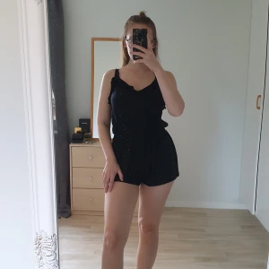 Svart jumpsuit - Använd en gång. Volang upptill. Knutit knut på axelbanden då dem är ganska långa för mig, lätt att sy in dem med några stygn. Passa S/M