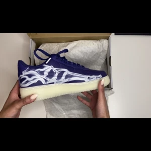 Nike air force 1 low 07 QS purple skeleton halloween (2021)  - Efterfrågade skor i marknaden. Säljs exklusivt för detta pris på Plick, däremot ligger de vanligtvis på 3000kr i vår webbplats. Köpare står för frakten. Alla skor går igenom äkthetscheck och vi garanterar att skorna är autentiska. 
