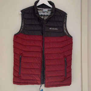 Columbia täckväst - Columbia. Väst med ”omni-heat”, mkt värmande. Vinröd/svart med silvrigt foder. Oanvänd. 