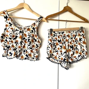 Mönstrat set  - Kort linne och korta shorts. Svart och tätt mönstrad med prästkragar. Små pompomfransar längs nedre kant. Den är inte vågig, den behöver bara strykas. 