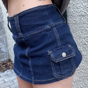 Y2K-inspirerad jeanskjol - Kort, mörkblå jeanskjol med inbyggda shorts under, så det gör ingenting att den är kort! Riktigt tuff kjol med detaljer och fickor, bra kvalitet och bekväm.