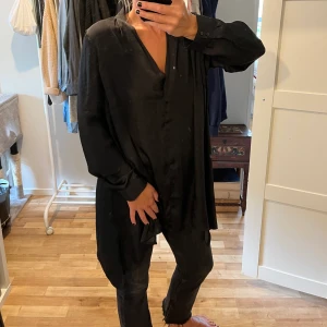 Svart tunika/blus - Lång svart tunika/blus i satin. Slitsar i sidorna. Stl 44, men på mig som har 38 blir den mer som en härlig tunika.