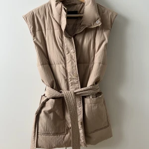 Beige väst - Jättefin väst köpt i Vero Moda. Den har midje band, dragkedja och knappar. Stora rymliga fickor. Skönt material och passar till allt! Brukar ha S men denna passar trots XS