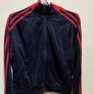 Adidas Track Top - Adidas Track Top i färgen mörkblå och röd. Köpt i Adidas butik på Freeport för ca ett år sedan, i nypris 400. Storlek S (34-36) Funkar för både tjej och kille. Lite kort i modellen. Använd 2-3 gånger så i princip ny. Inga skador eller liknande.