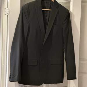 En stilig svart kostym med väldigt tunna gråa linjer i stl 50. Använd endast en gång. Kostymen består av kavaj och slimmad byxa. Mycket elegant. 
