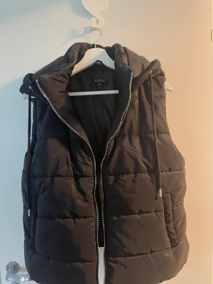 Svart väst strl M - Väst med luva i storlek M, passar S mer. Från Boohoo. Liten fläck på sidan(se bild 3), men den ska gå att tvätta i tvättmaskin. Pris kan diskuteras