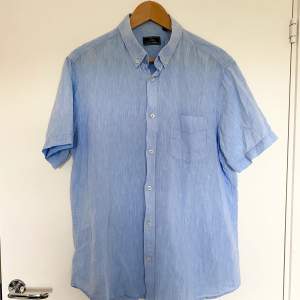 Ljusblå kortärmad skjorta. Material: 55% linne, 45% bomull. Köpt begagnad i mycket bra skick, aldrig använt själv.