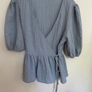 Ljusblå blus  - En jättefin ljusblå blus från NA-KD, puffar på ärmarna, omlottblus. I mycket fint skick, använd några få gånger! I storlek 36.  Kan skickas om så önskas! 