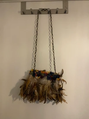 Axelremsväska i fjädrar - Söt axelremsväska, nästan helt oanvänd. Kedja som axelrem och täckt av fjädrar och blommor