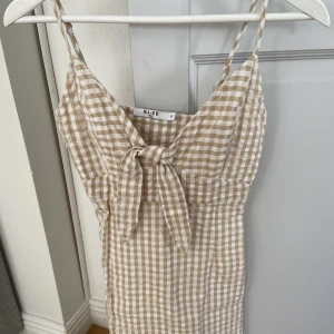 Vit och beige rutig klänning - Beige och vit rutig miniklänning från NAKD. I strl 34. I linnematerial typ, fin knytdetalj framtill. Använd fåtal gånger!