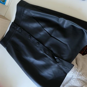 Svart kjol - Svart kjol i fejkskinn, mycket fint skick! Svarta knappar. 