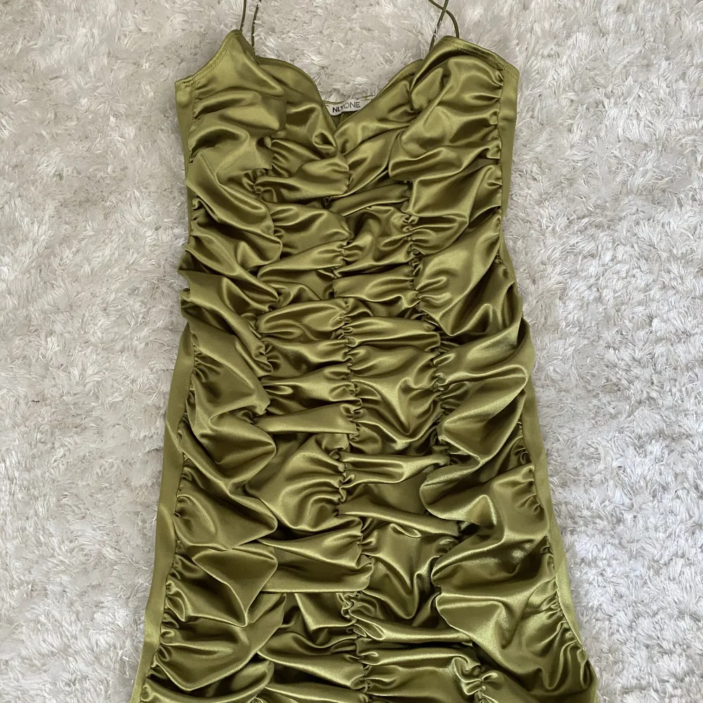 Grön/olivgrön mini klänning som har snyggt rynkat mönster på framsidan och slät på baksidan från Nelly. Aldrig använd. Klänningar.