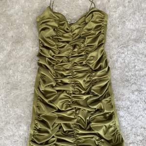Grön/olivgrön mini klänning som har snyggt rynkat mönster på framsidan och slät på baksidan från Nelly. Aldrig använd