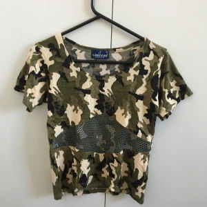 Topp med camomönster - Supercool topp/t-shirt, min syrras i fint skick. Perfekt i sommar! Camomönstrad och har en nätdetalj tvärs över. Märkt XL men definitivt mindre, passar fler storlekar pga stretchig! Mått mellan armhålorna 36,5 cm, längd 45 cm. Skriv för fler bilder!