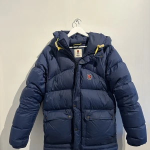 Fjällräven Jacka - Fjällräven jacka i färgen marinblå, Storlek Medium (mensize), utmärkt skick, lilla spännet på sista bild har format sig lite men inget som märks, nypris 6999kr, mitt pris 3500kr