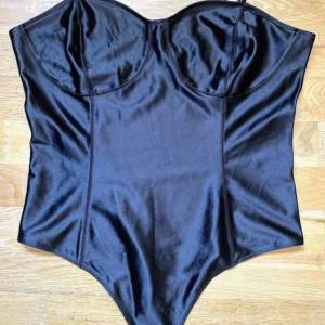 Superfin body/top i svart glansigt stretchigt material. H&M Ställbara axelband & knäppnings grenen Som ny! Endast provad Passar perfekt till ett par jeans eller en kjol!