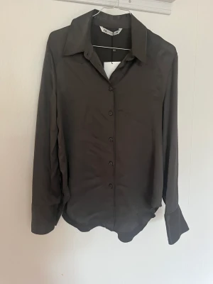 Mörkgrå satinskjorta - Skitsnygg satinskjorta från Zara! Säljes pga lite för liten i ärmarna för mig. Passar en S/M. Aldrig använd! 