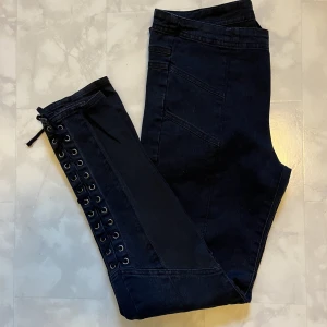 Svarta jeans med detalj - Jeans med snörning längs benen. Tunnt och skönt material. Stretchigt tyg vid vaderna. ”M”, men de är små i storleken! Jag får de inte över låren, så skulle säga att de är närmare S. Lite korta i benen. Tror de lämpar sig bäst för en kortare/mindre person.