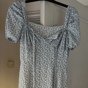 Lång klänning - Lång ljusblå klänning med blomtryck, strlk L men den är lite liten så funkar nog med M också. Deagkedja finns på sidan. 