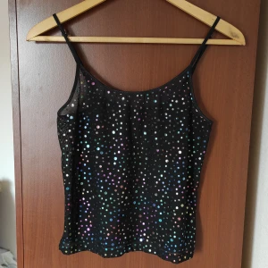 Vintagetopp med paljetter - Snygg topp med vintagefeeling. Färg: svart med paljetter i flera färger. Skick: använd. Paljetterna vid bysten har förlorat lite färg, men annars i bra skick(se bild 3). Material: 80% polyester och 20% elastan. 